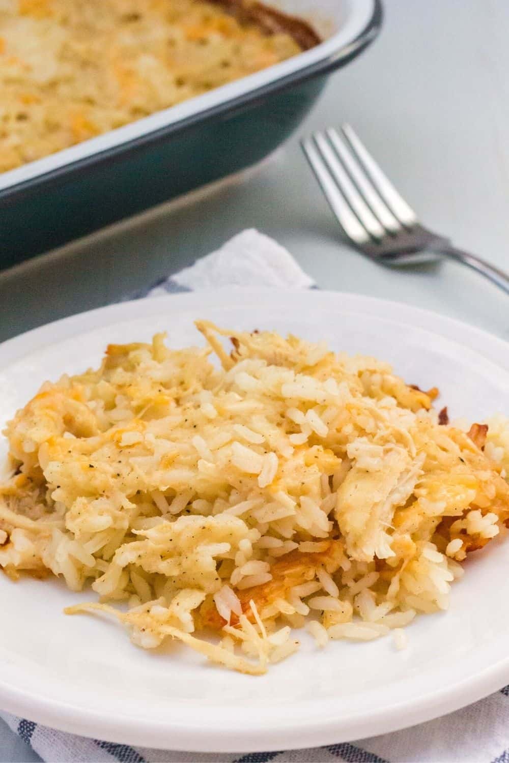 close-up view of cheesy no-peek chicken and rice served on a plate, with the baking dish in the background.