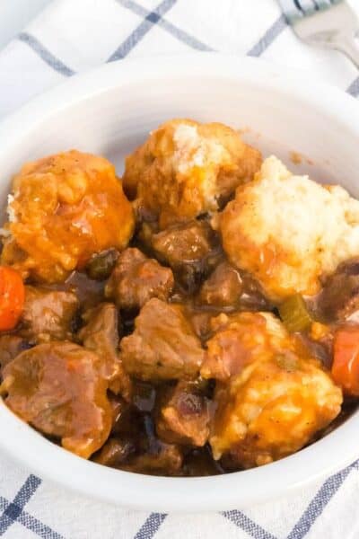 a white bowl serves homemade beef stew and dumplings. A fork is next to the bowl.