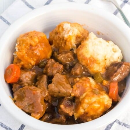 a white bowl serves homemade beef stew and dumplings. A fork is next to the bowl.