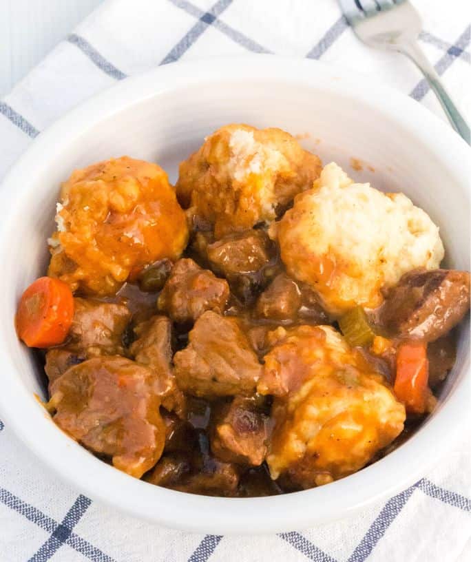 a white bowl serves homemade beef stew and dumplings. A fork is next to the bowl.