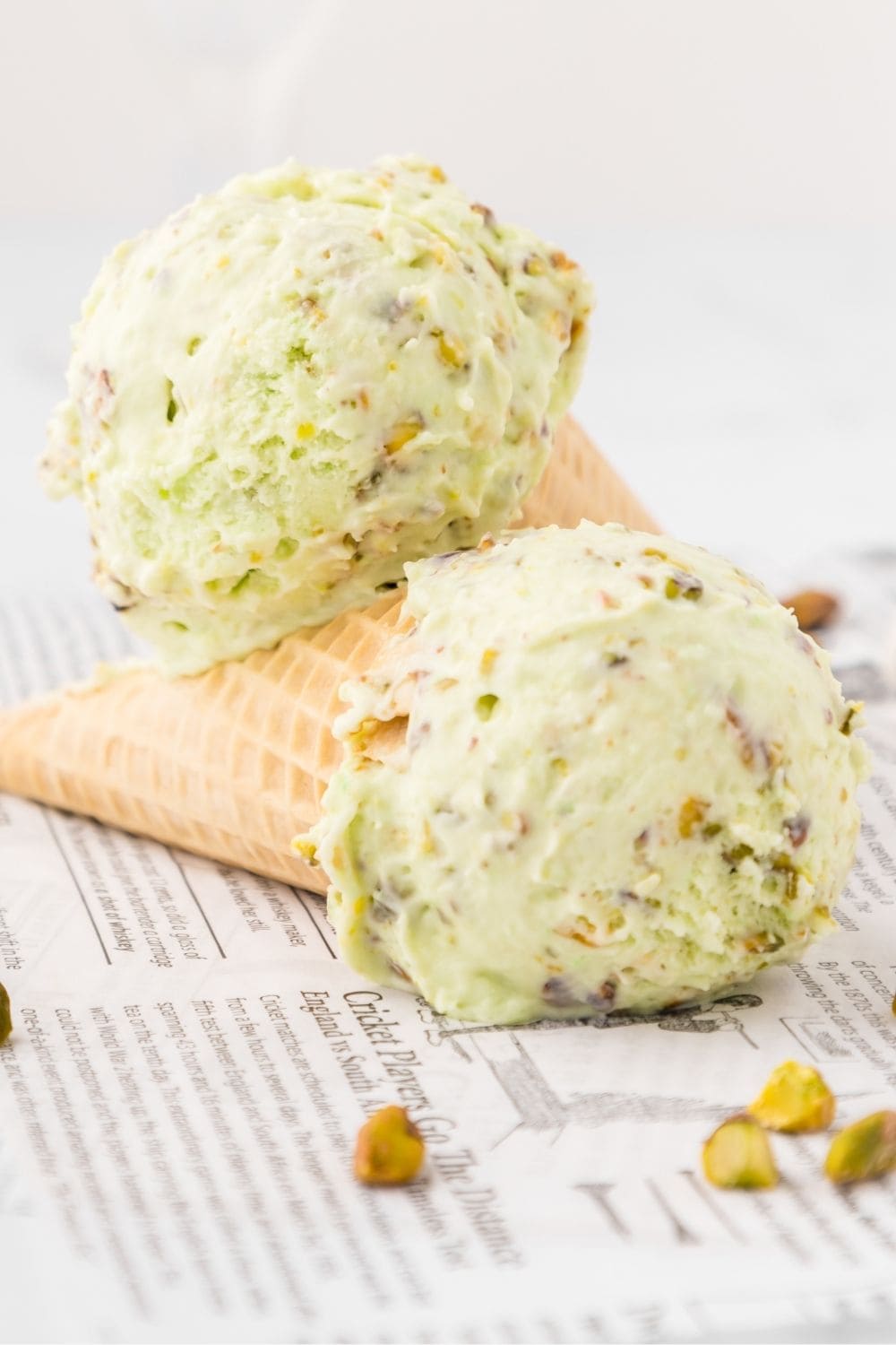 two ice cream cones with scoops of pistachio ice cream made without an ice cream machine resting on each other.