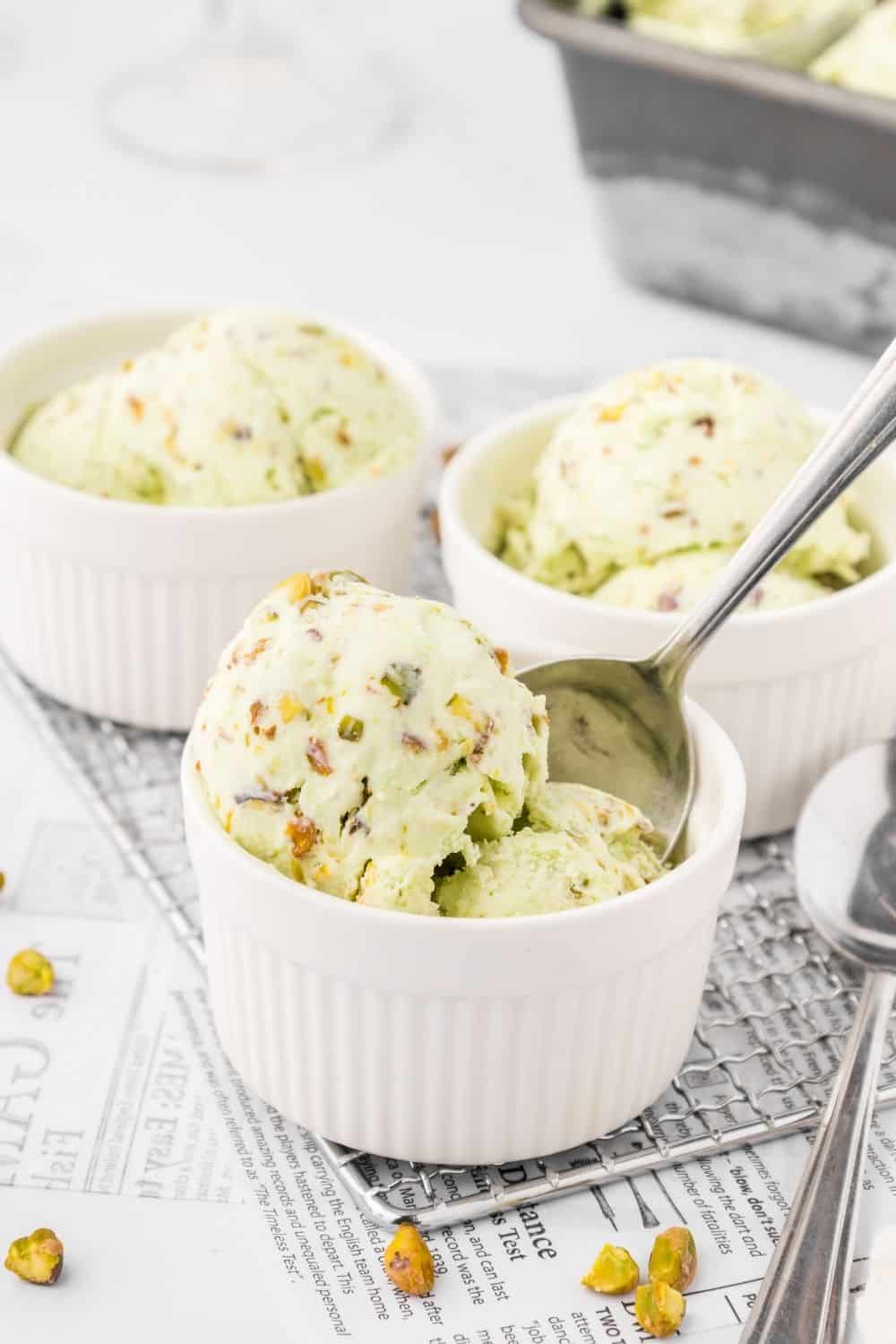 three small white bowls serve scoops of homemade pistachio ice cream. A spoon is in one bowl.