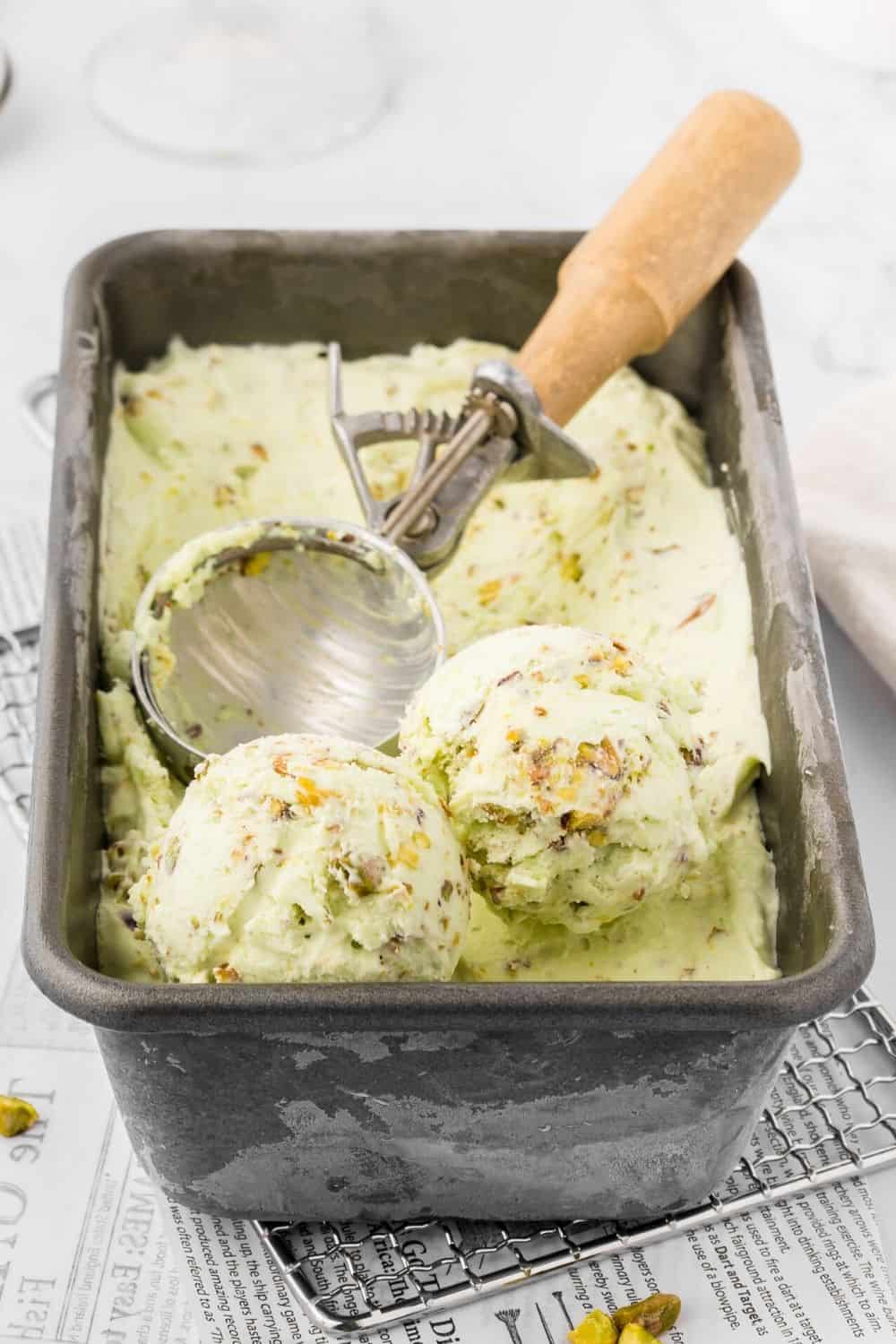 scoops of eggless homemade pistachio ice cream on the surface of the ice cream container.