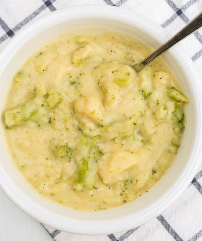 close-up view of a white bowl of homemade broccoli potato soup with cheese.