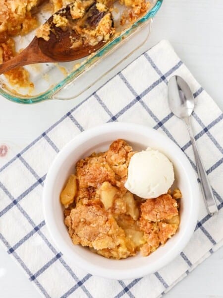overhead view of a white bowl serving cake mix pear cobbler a la mode, with the baking dish of cobbler in the background.