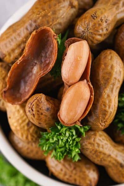 close-up view of a bowl of stove top boiled peanuts, with one peanut shell opened to show the tender peanuts inside.
