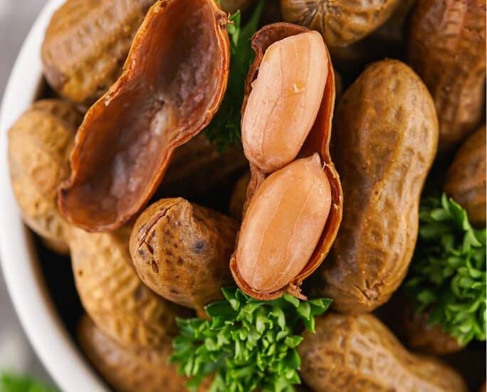 close-up view of a bowl of stove top boiled peanuts, with one peanut shell opened to show the tender peanuts inside.