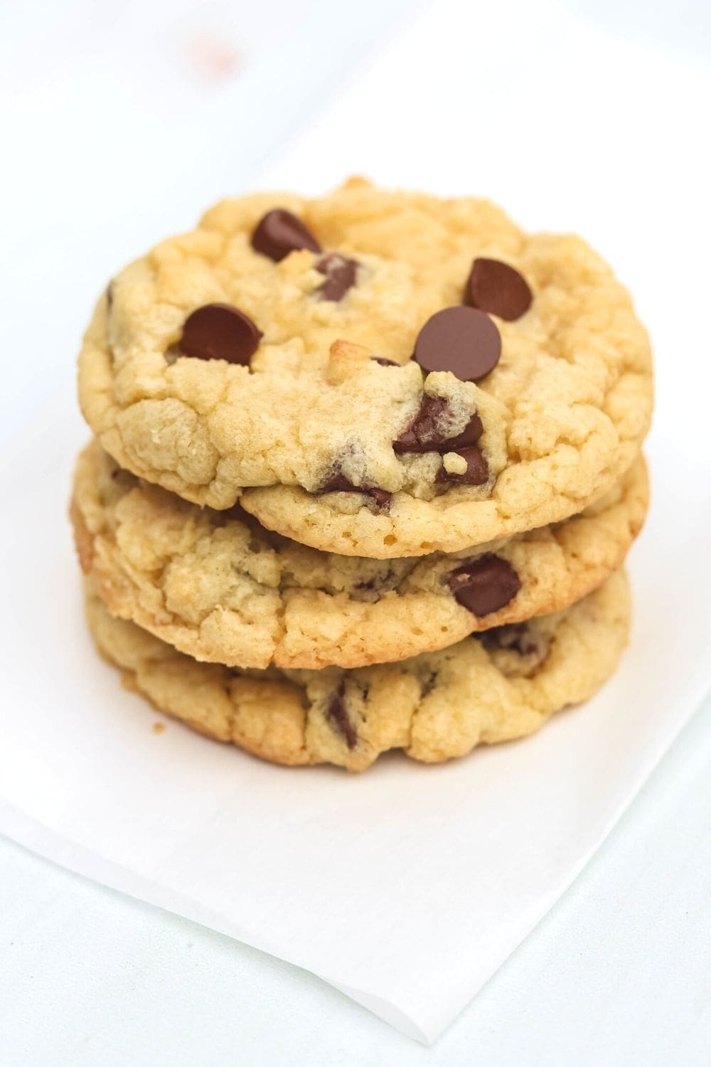 close-up view of a stack of three soft and chewy Bisquick chocolate chip cookies on a piece of parchment paper