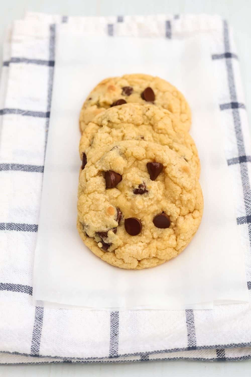 three chocolate chip Bisquick cookies on a piece of parchment paper, atop a blue and white napkin