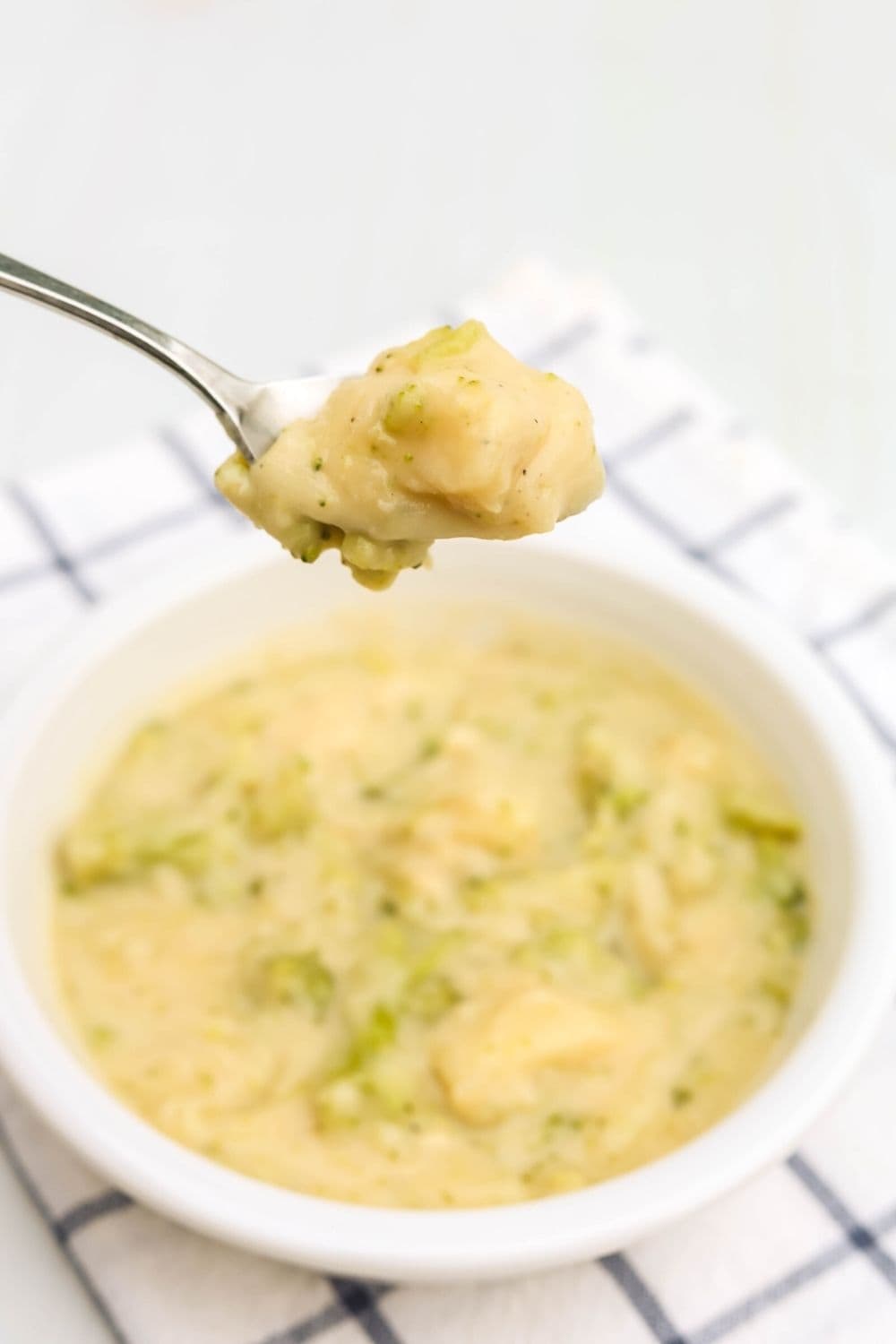 chunky broccoli potato soup on a spoon, with the bowl beneath it.