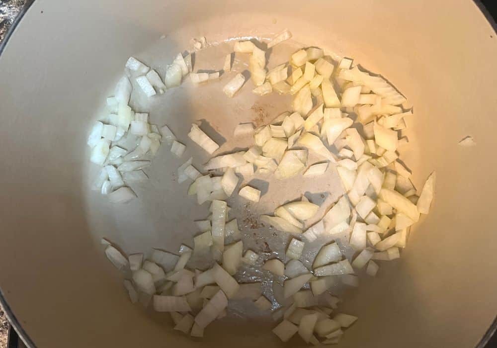overhead view of diced onions being sauteed in olive oil in a dutch oven.