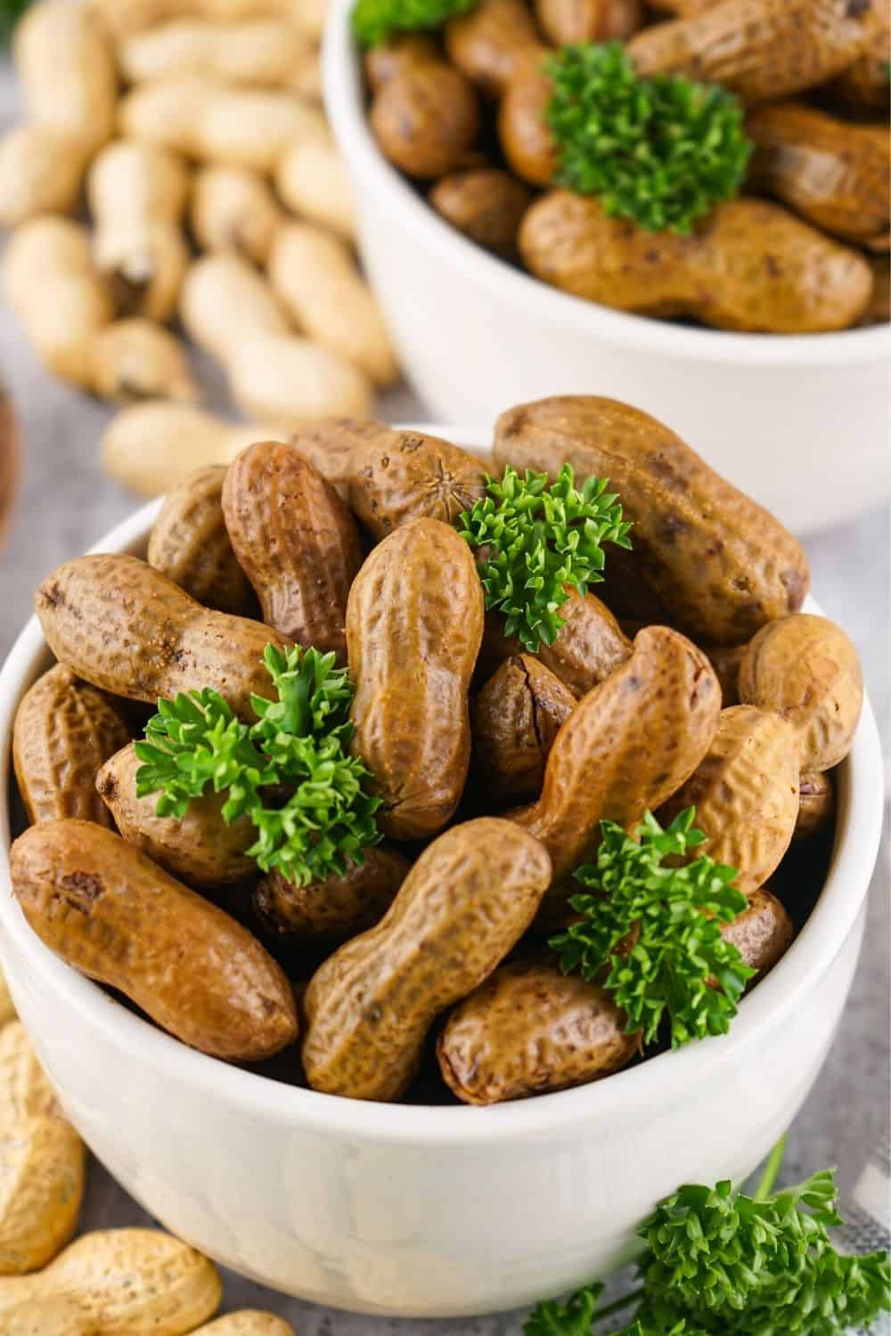 two white bowls of boiled peanuts are garnished with fresh parsley