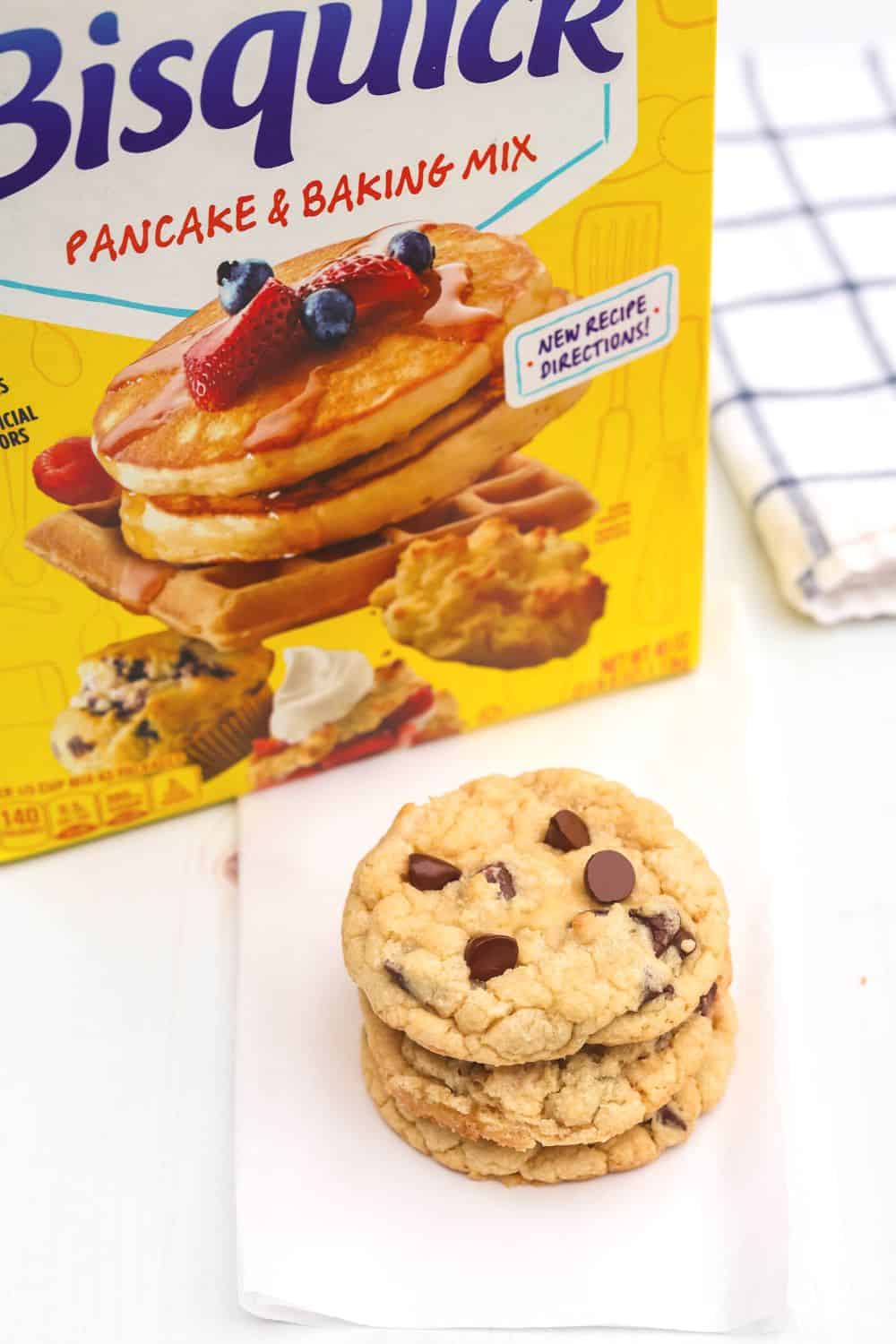 three chocolate chip cookies are stacked in front of a box of Betty Crocker Bisquick baking mix