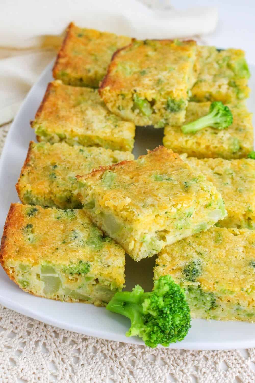 a white platter serves pieces of Jiffy broccoli cornbread with cheese. The platter is garnished with pieces of broccoli.