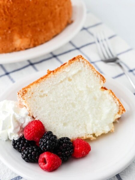 slice of the best angel food cake from a mix, served on a white plate with fresh berries and whipped cream.