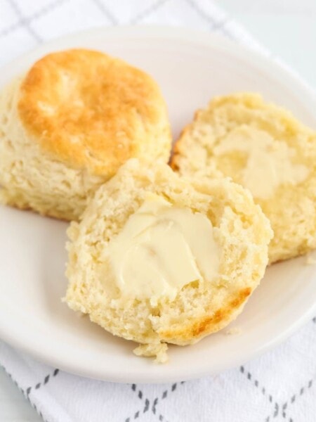 two Bisquick biscuits on a white plate; one is cut in half and spread with butter.