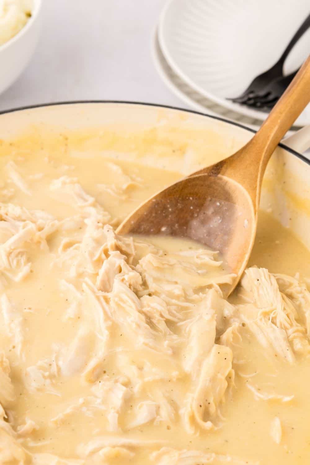 a wooden spoon stirs a pan of stove top chicken and gravy that's ready to be served
