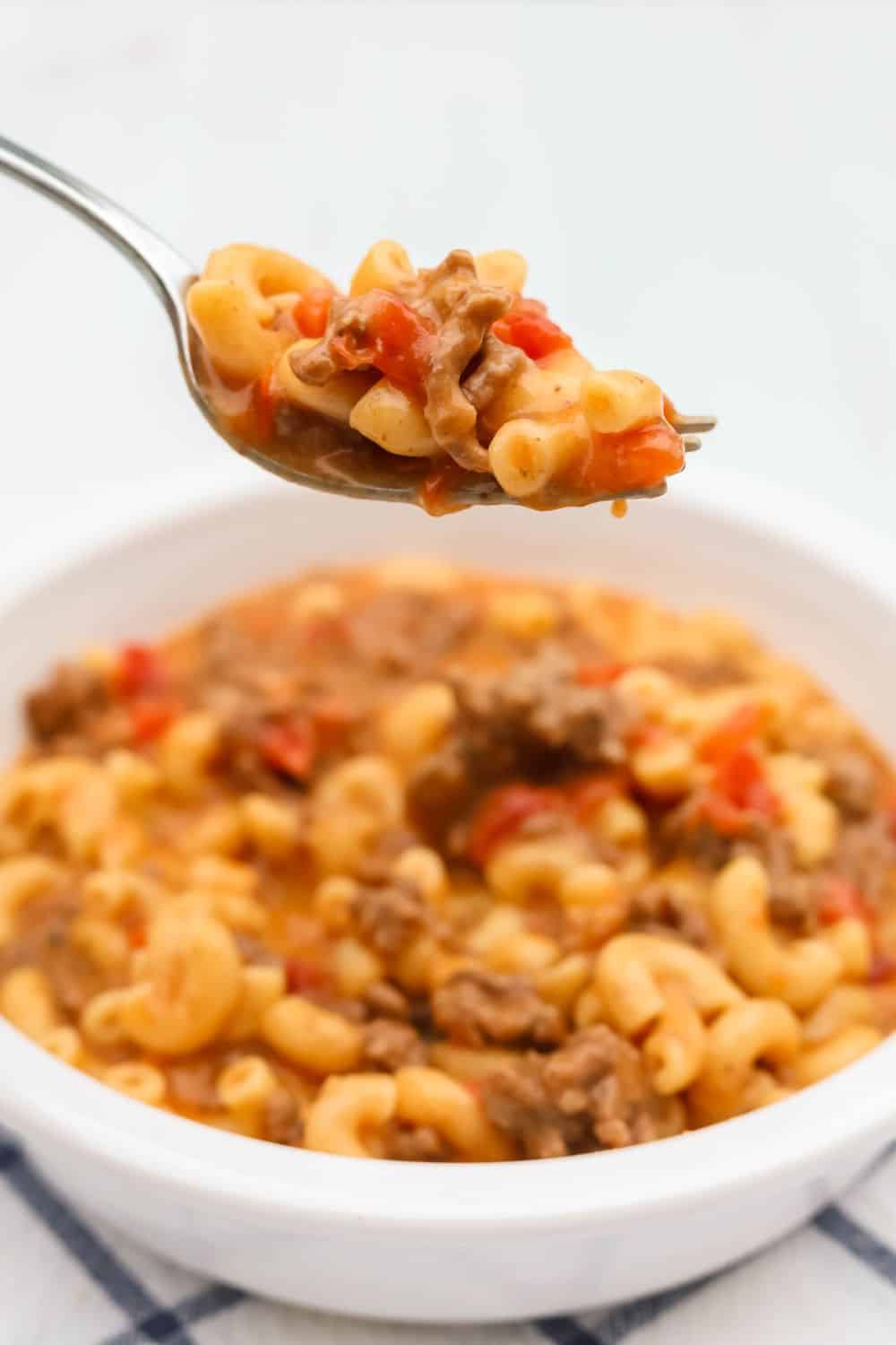 a fork lifts a bite of cheeseburger macaroni made in the Instant Pot out of a bowl serving the same.