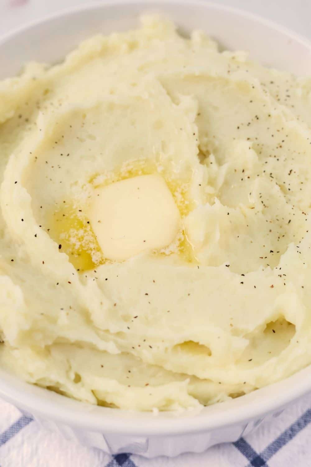 close-up view of fluffy, creamy mashed potatoes made in the instant pot, topped with salt, pepper, and butter. 