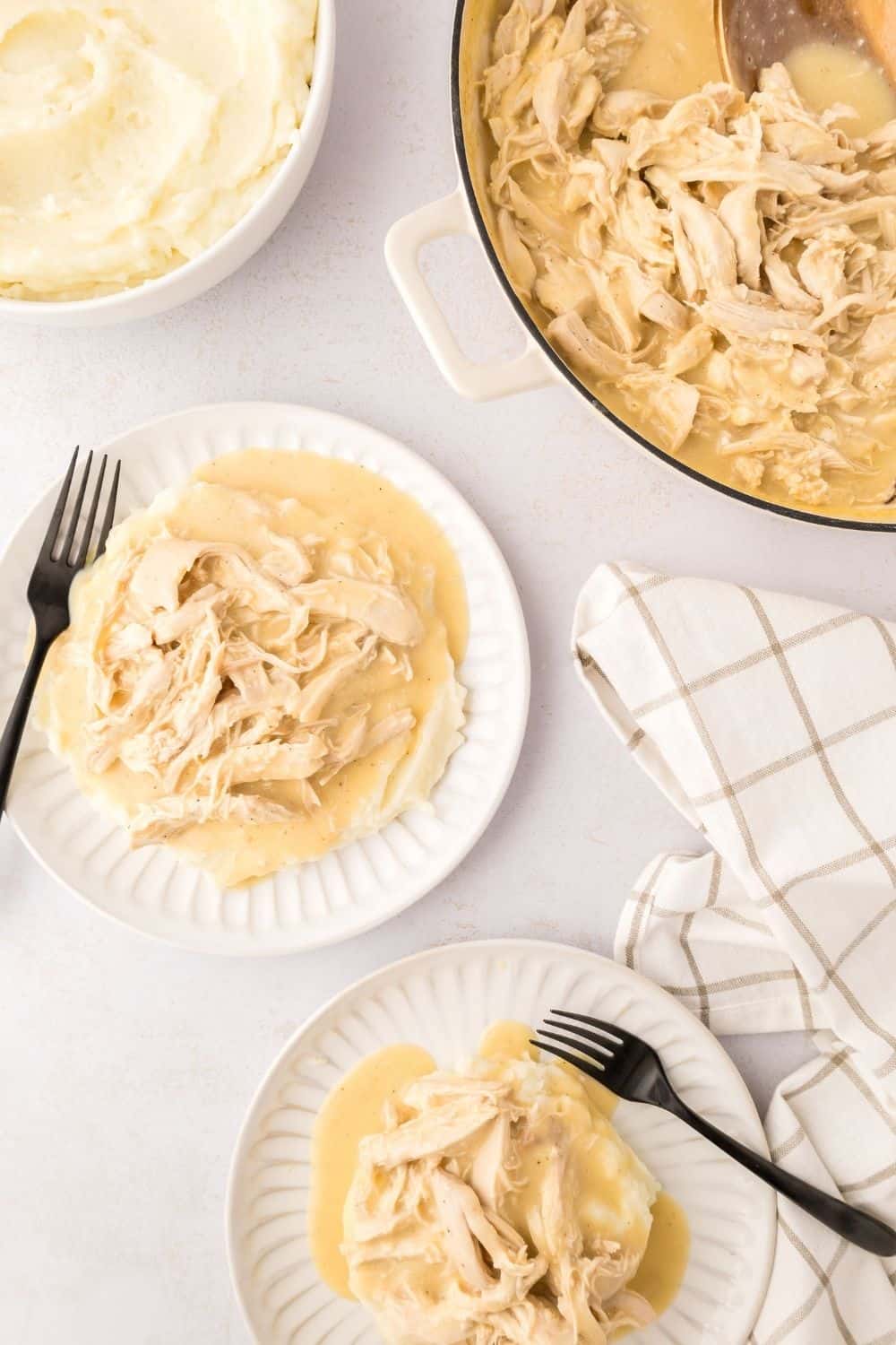 overhead view of white plates serving shredded chicken and gravy over mashed potatoes, with the skillet in the background.