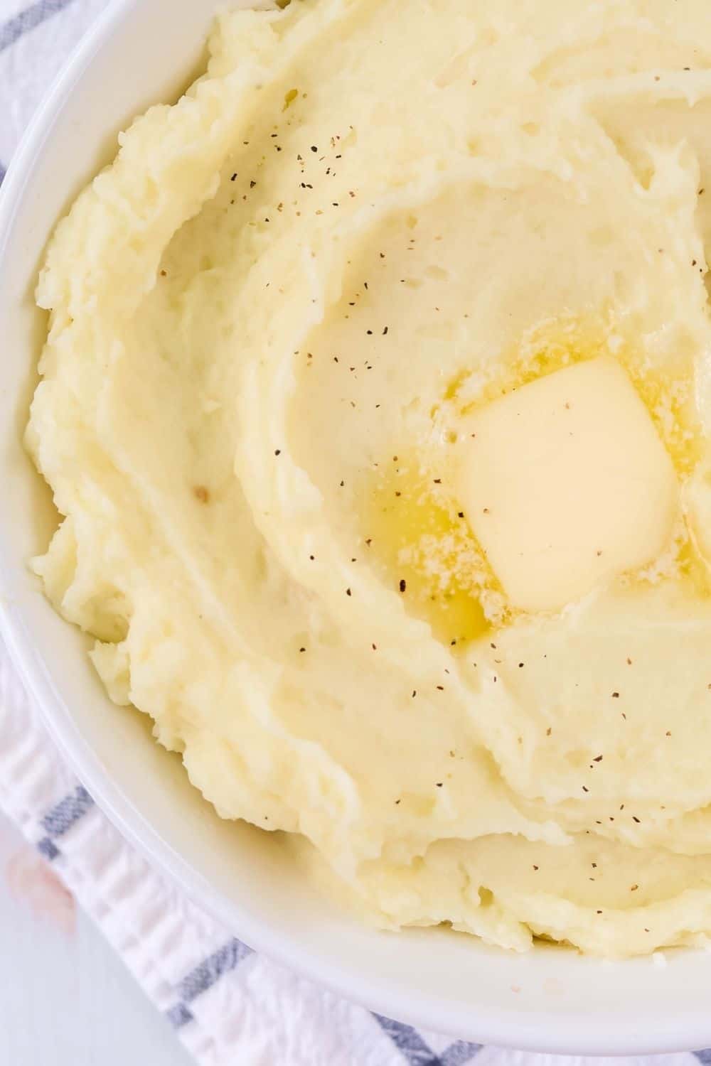 close-up view of pressure cooker mashed potatoes in a white bowl, with salt, black pepper, and melted butter on top.