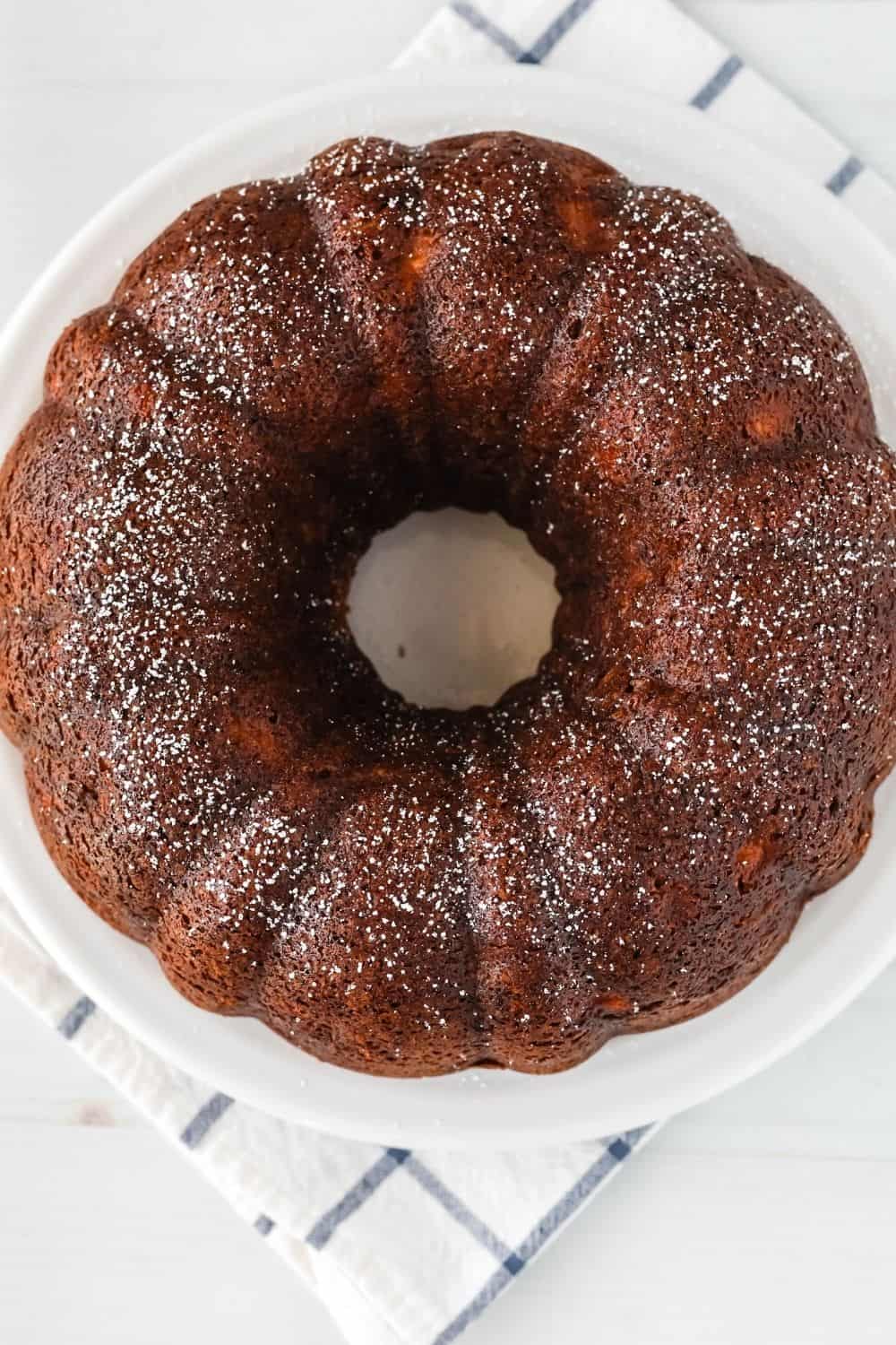 overhead view of a pear and banana bundt cake on a white serving plate, dusted with powdered sugar.