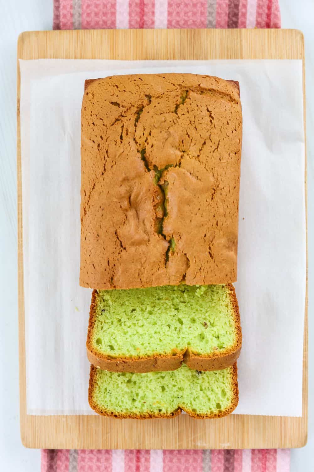 overhead view of a loaf of pistachio bread made with pudding mix, which is partially sliced on a cutting board, displaying the green slices that are perfect for holidays.
