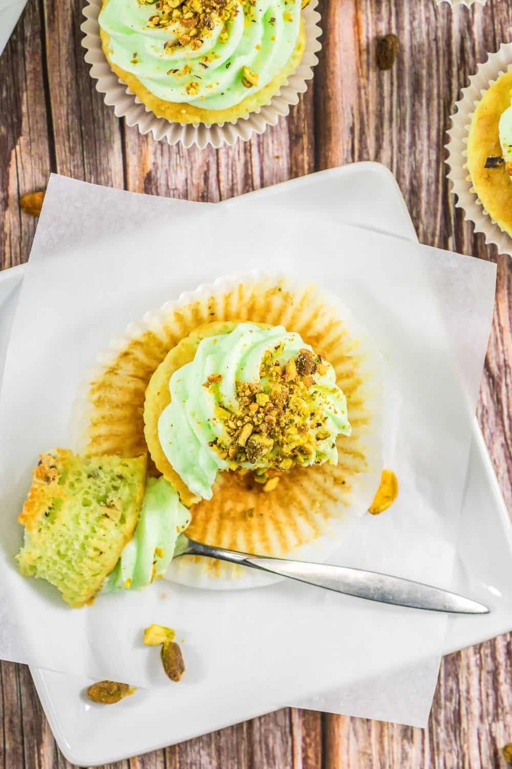 overhead view of a cake mix pistachio cupcake on a white plate, with a bite taken out of it by a fork that's resting next to it.
