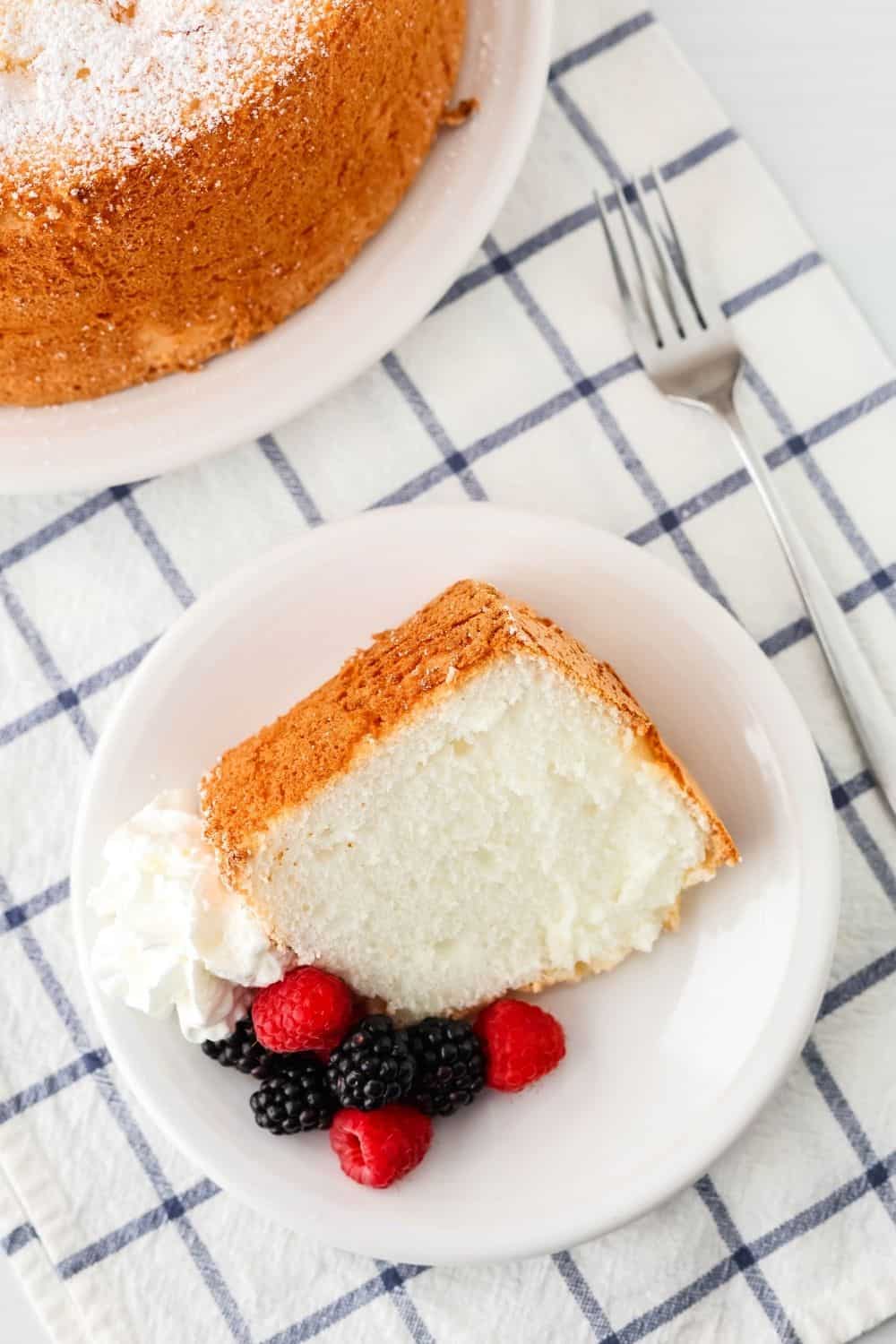 overhead view of a slice of angel food cake with berries and cream on a white plate, showing the fluffy interior.