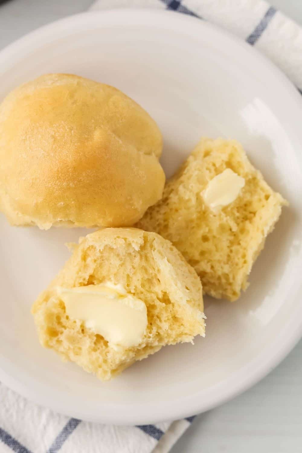 overhead view of dinner rolls that were proofed in the instant pot. One is sliced open and spread with butter, showing the fluffy interior.