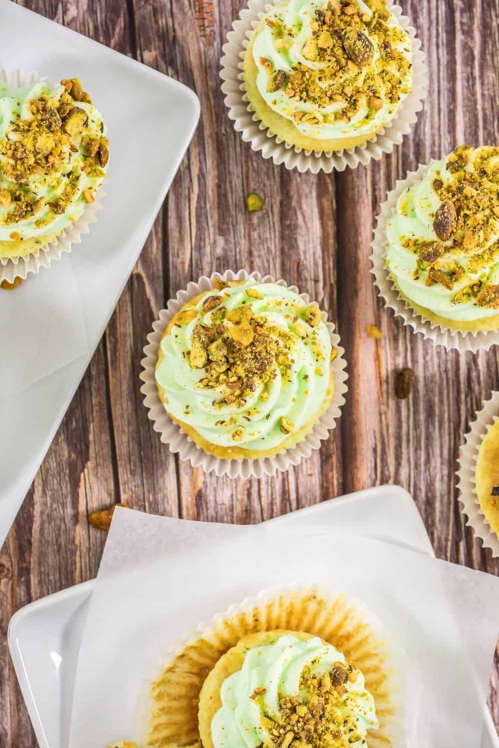overhead view of several homemade pistachio cupcakes scattered on a wooden table.