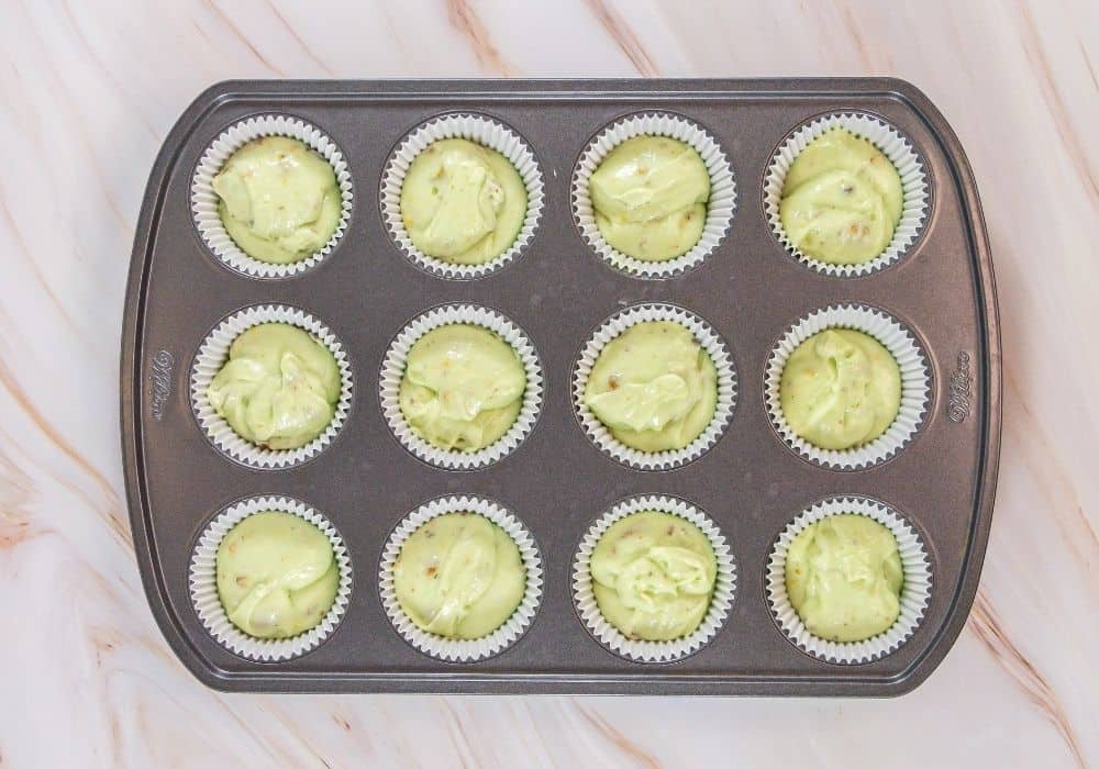 pistachio cake batter added to cupcake liners in a muffin pan, prior to baking.
