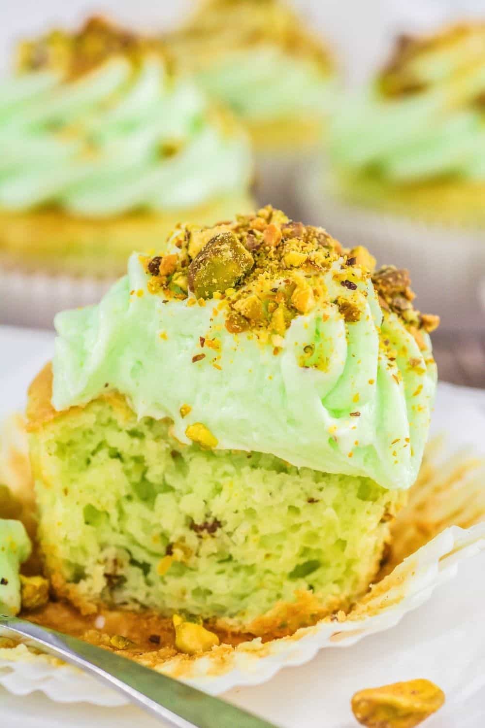 close-up view of a pistachio cupcake that's been cut in half, showing the moist interior and the creamy pistachio buttercream frosting.
