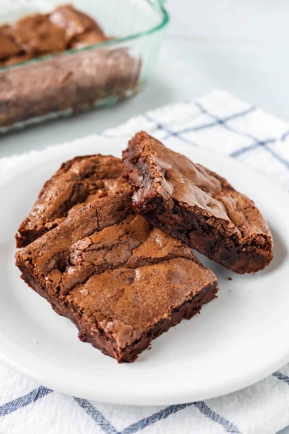 close-up view of a few Bisquick baking mix brownies served on a white plate, with the remaining pan of brownies in the background.