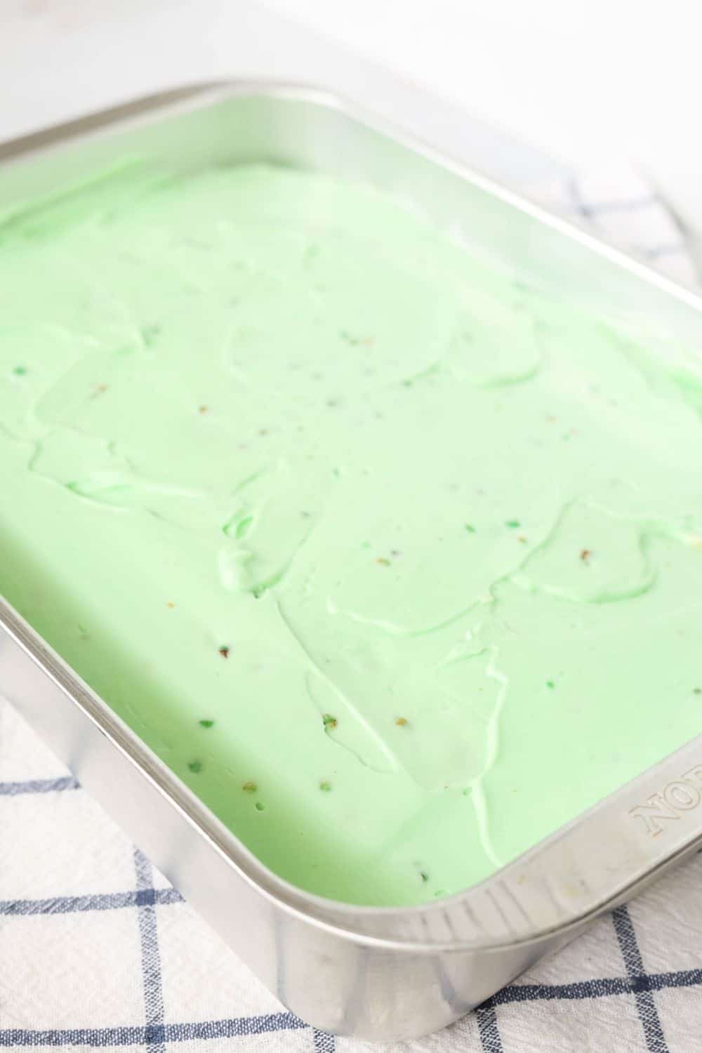 angled view of an aluminum 9x13" pan with a frosted pistachio cake in it.