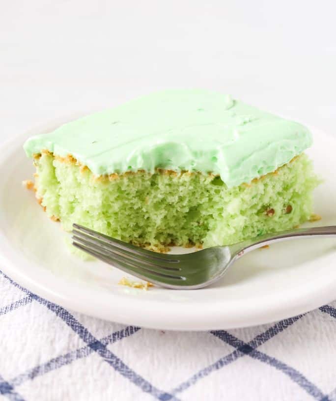 a slice of pistachio sheet cake made with cake mix and pudding mix, served on a white plate. A bite has been taken out of the cake and a fork is next to the slice.