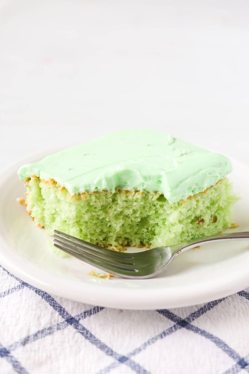 a slice of cake mix pistachio sheet cake on a white plate, with a bite taken out of it and a fork next to it.