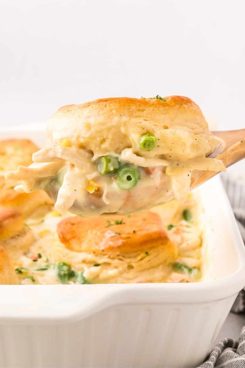 side view of a wooden serving spoon scooping out chicken pot pie with Pillsbury Grands biscuits.