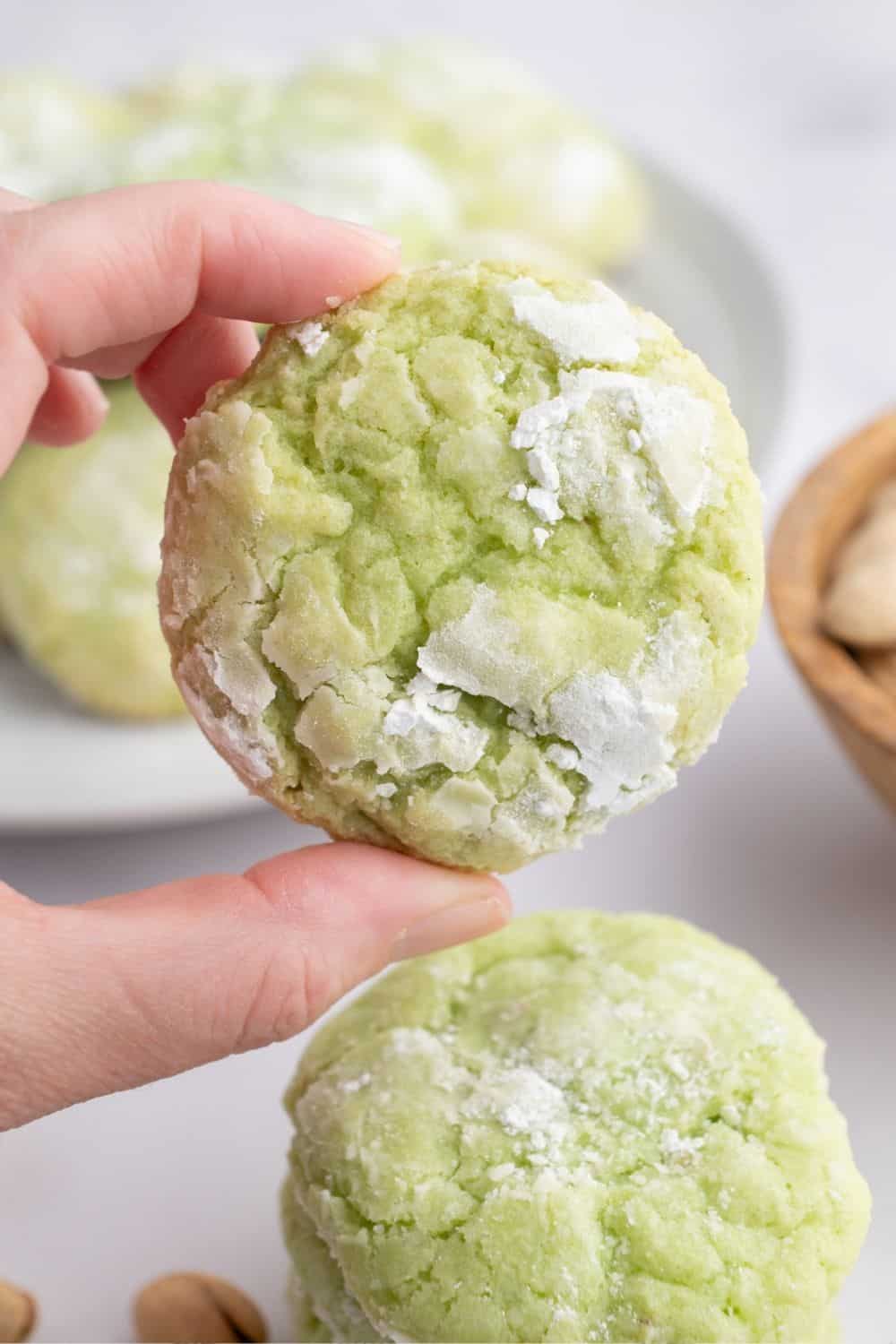a woman's hand holds a pistachio crinkle cookie, showing the crinkly pattern on the top.