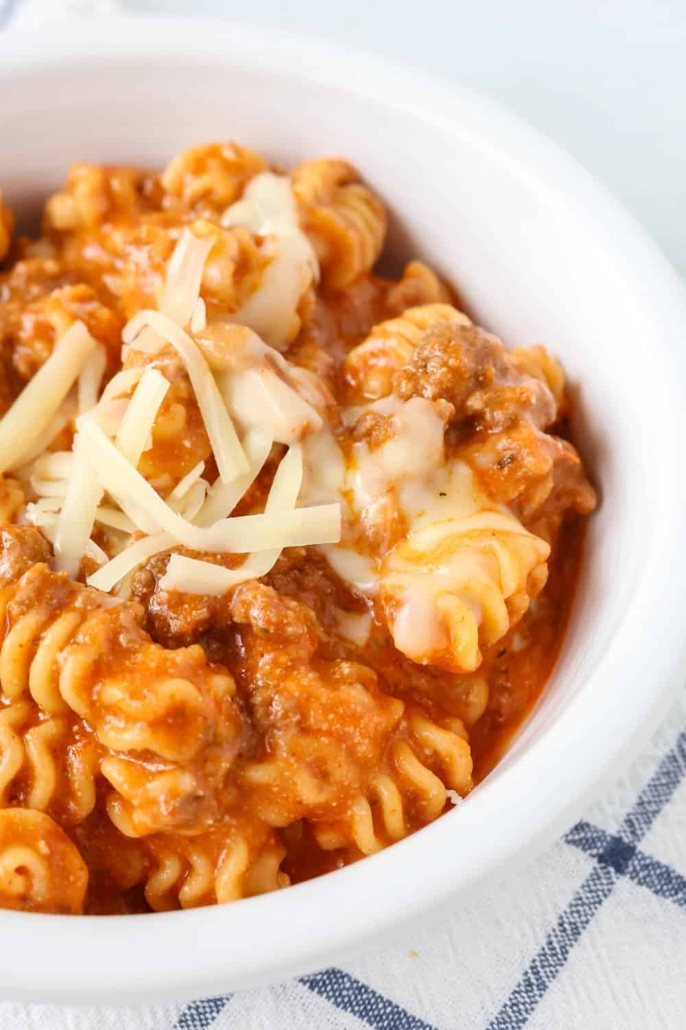 close-up detailed view of instant pot lasagna casserole served in a white bow. It's made with noodles, ground beef, marinara sauce, ricotta cheese, and mozzarella cheese.