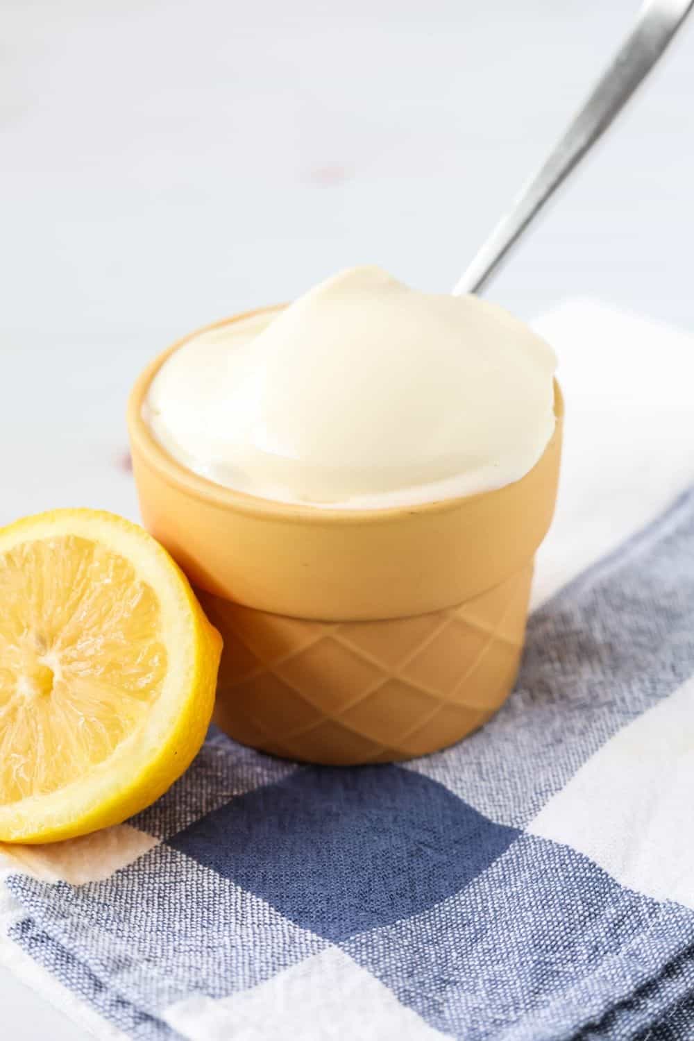 close-up side view of lemon gelato served in a dessert cup, showing how silky smooth the gelato is. A spoon is in the ice cream, and a lemon half is next to it.