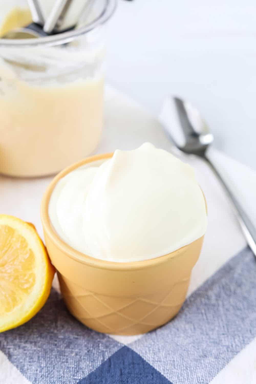 an ice cream cone-shaped dish serves a helping of lemon gelato made in the Ninja Creami. The pint of remaining gelato is in the background, along with a spoon.