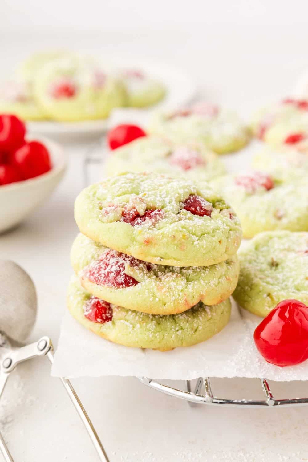 a few pistachio pudding cookies full of maraschino cherries, stacked on a wire cooling rack.