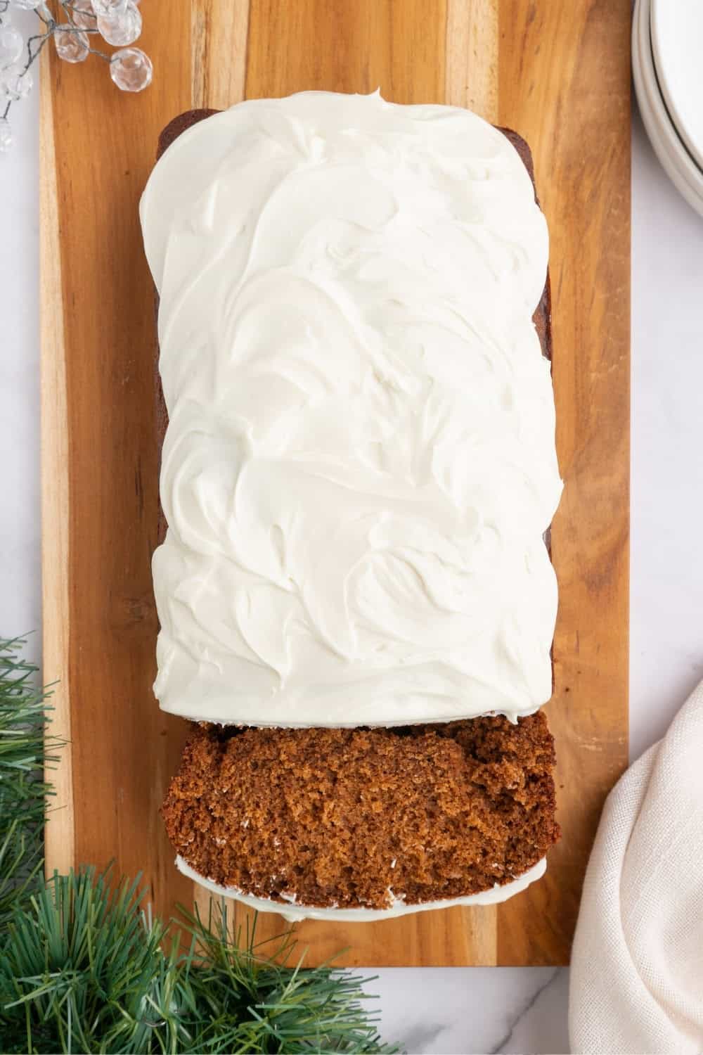 overhead view of a loaf of gingerbread, topped with cream cheese frosting. A slice is cut from the loaf.