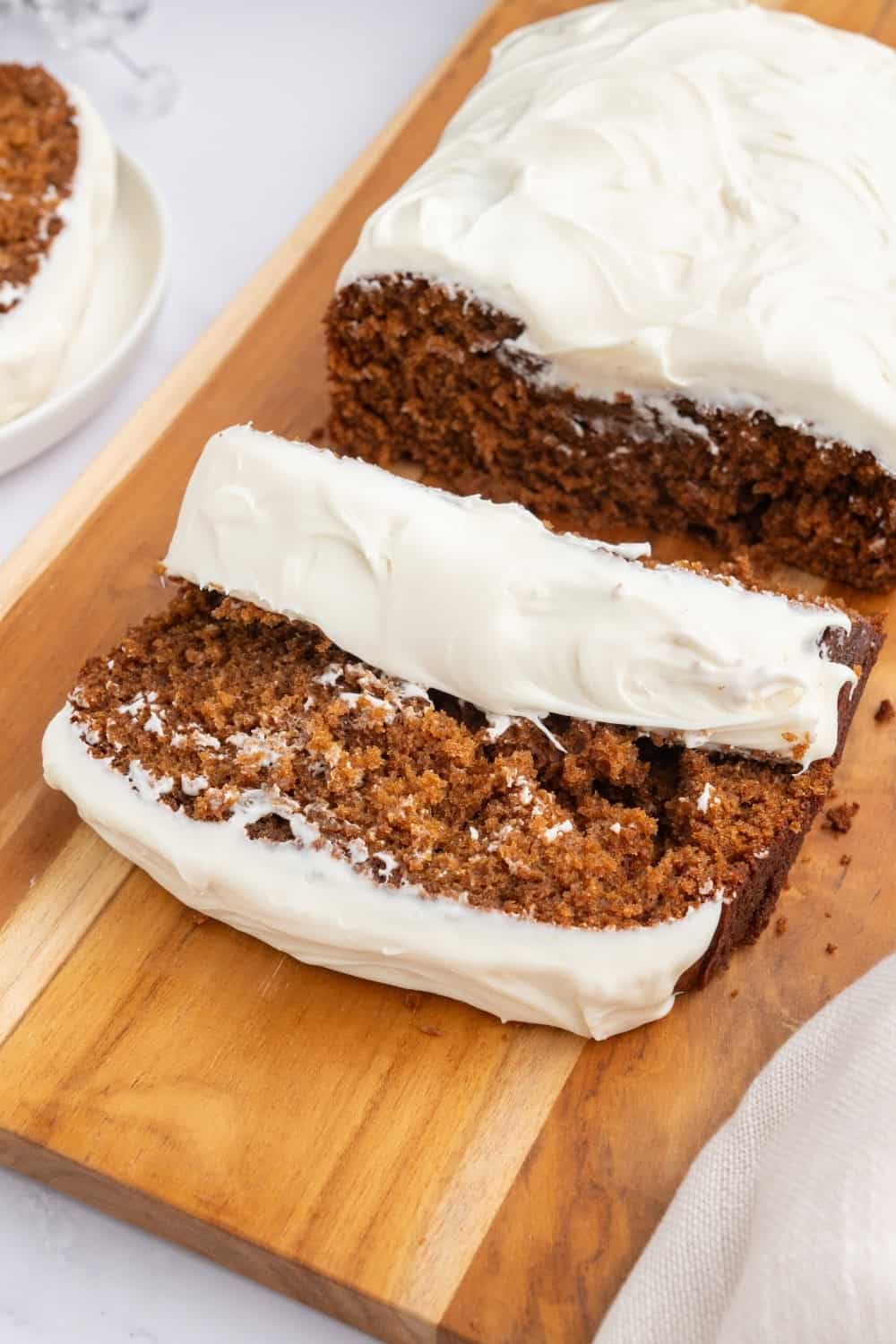 sliced holiday gingerbread loaf with cream cheese frosting, served on a wooden cutting board.