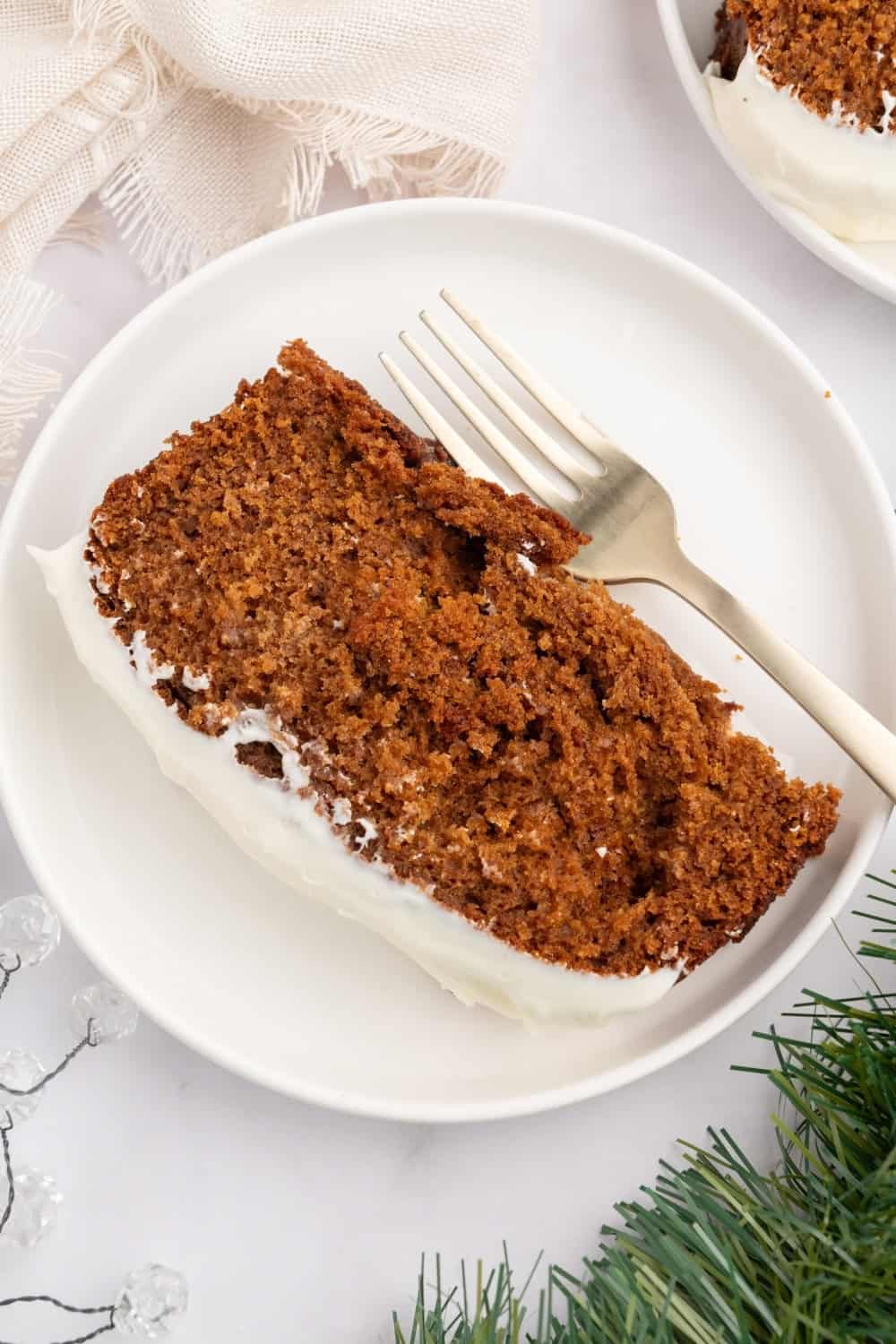 overhead view of a slice of homemade frosted gingerbread loaf cake on a white plate, with a fork next to it.