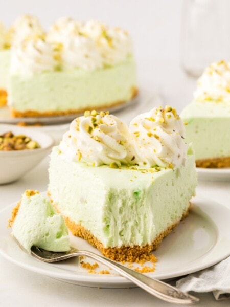 a slice of no bake pistachio cheesecake on a white plate, with a bite taken out of it.