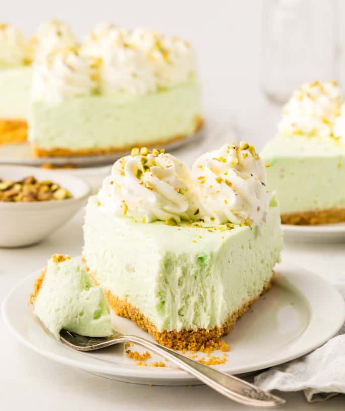 a slice of no bake pistachio cheesecake on a white plate, with a bite taken out of it.