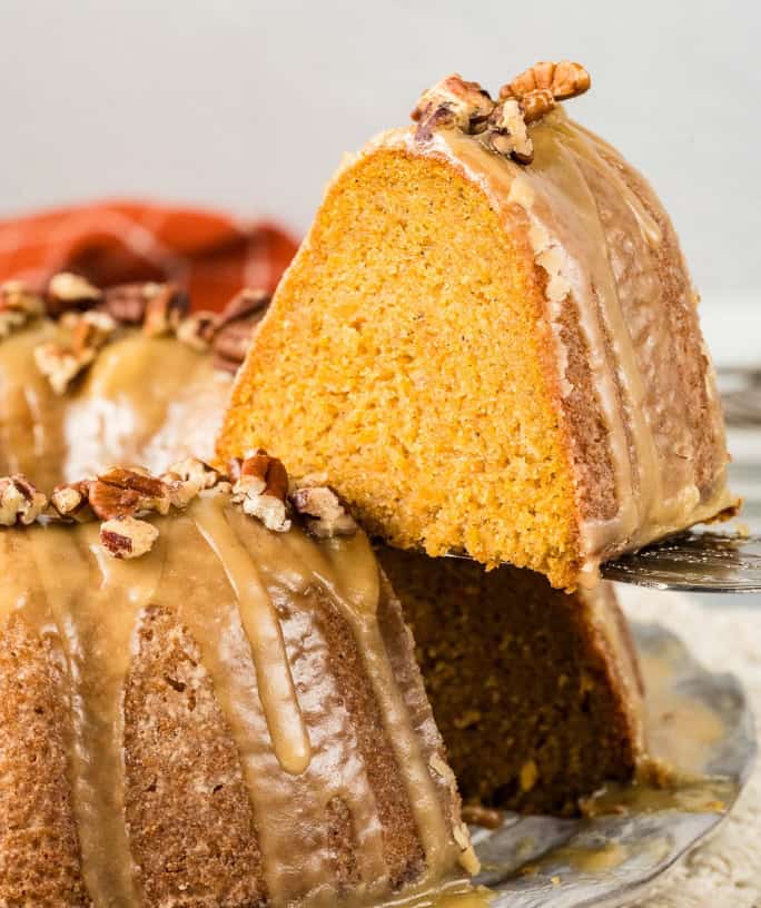 a slice of glazed sweet potato pound cake being lifted off the serving plate by a cake server.