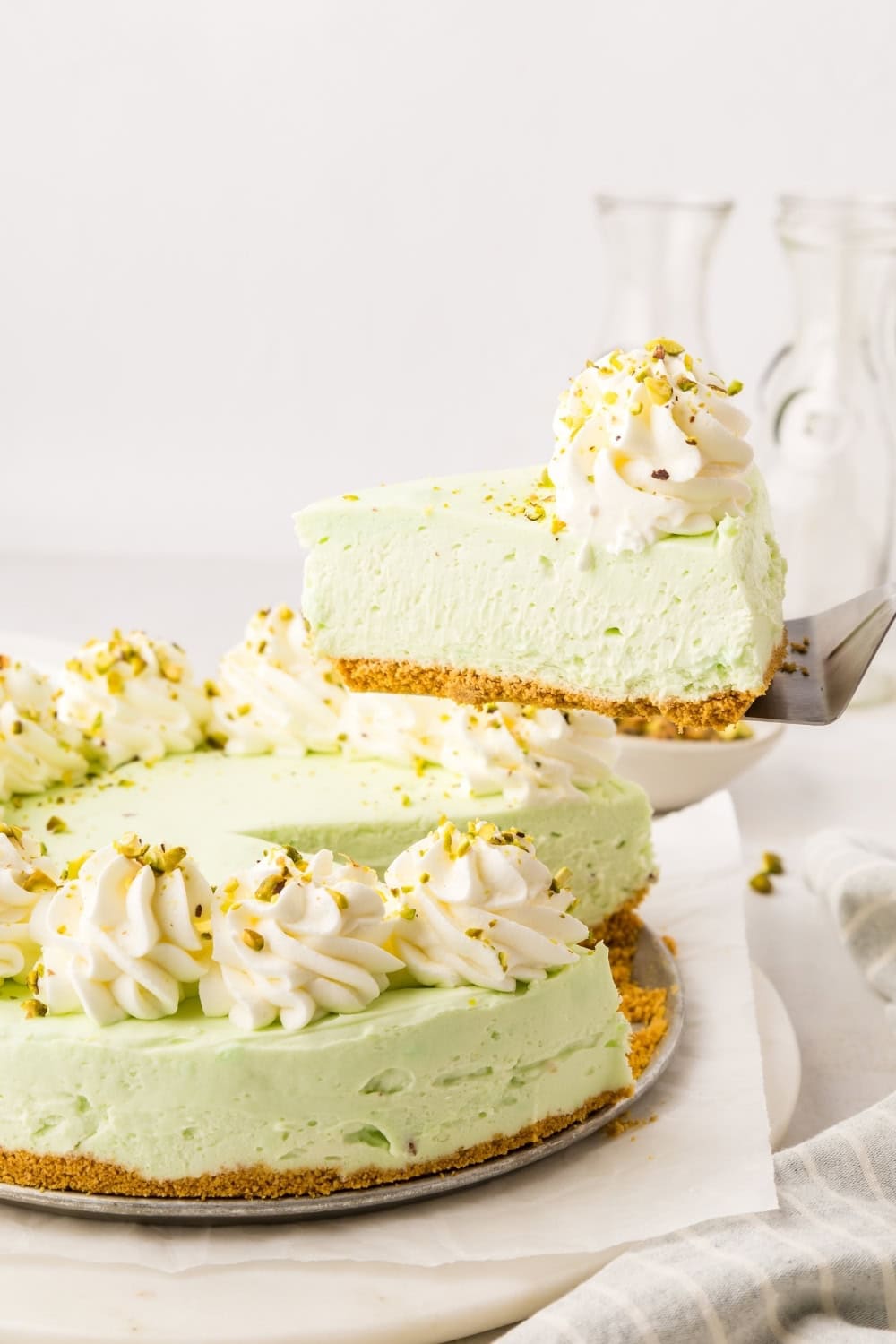 a pie server lifts a slice of pistachio cheesecake out of the pan for serving.